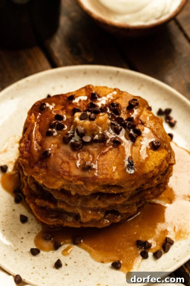 A glorious stack of fluffy whole wheat pumpkin pancakes, generously drizzled with cinnamon caramel syrup and sprinkled with mini chocolate chips, ready for a cozy fall breakfast.