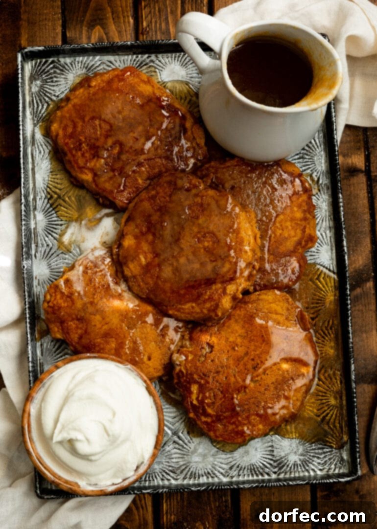 A warm sheet pan filled with golden whole wheat pumpkin pancakes, generously covered in glistening cinnamon caramel syrup, with a side bowl of whipped cream, inviting a delightful breakfast.