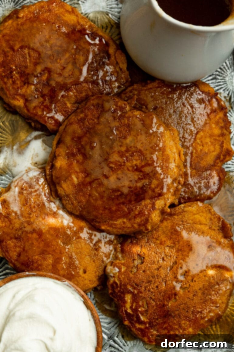 A festive spread of several whole wheat pumpkin pancakes on a baking sheet, glistening with cinnamon caramel syrup, accompanied by a bowl of freshly whipped cream and a carafe of extra syrup, perfect for a special breakfast.
