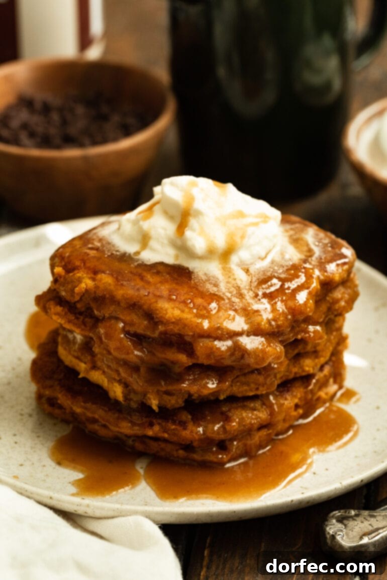 A pristine white plate holds a stack of golden whole wheat pumpkin pancakes, elegantly topped with glistening cinnamon caramel syrup and a dollop of melting butter, ready to be enjoyed.