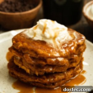 A stack of delicious whole wheat pumpkin pancakes sitting on a white plate topped with cinnamon caramel syrup and a dollop of melting butter.