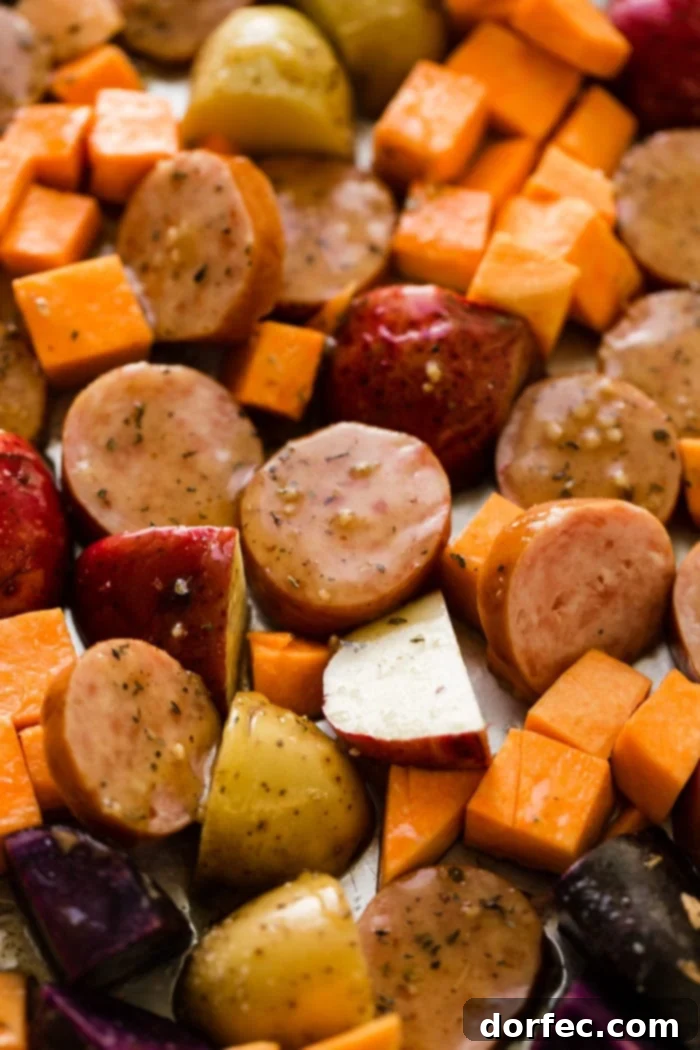 Uncooked sliced kielbasa and diced root vegetables arranged on a sheet pan, ready for the oven