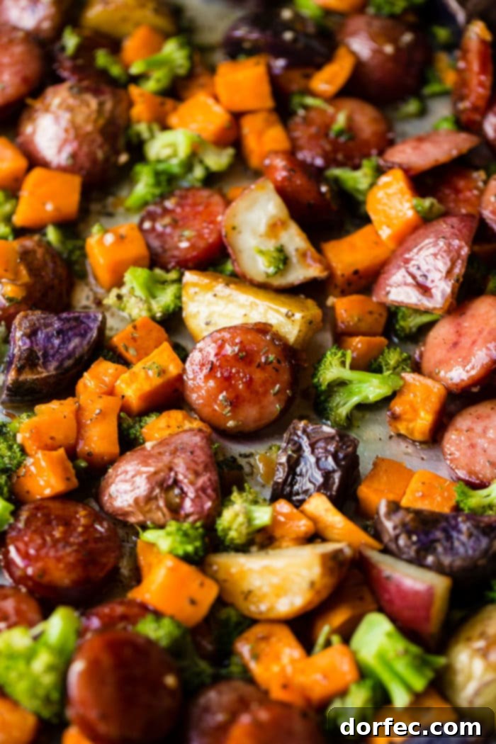 Close-up of roasted sliced kielbasa, sweet potatoes, and broccoli on a sheet pan, ready to serve