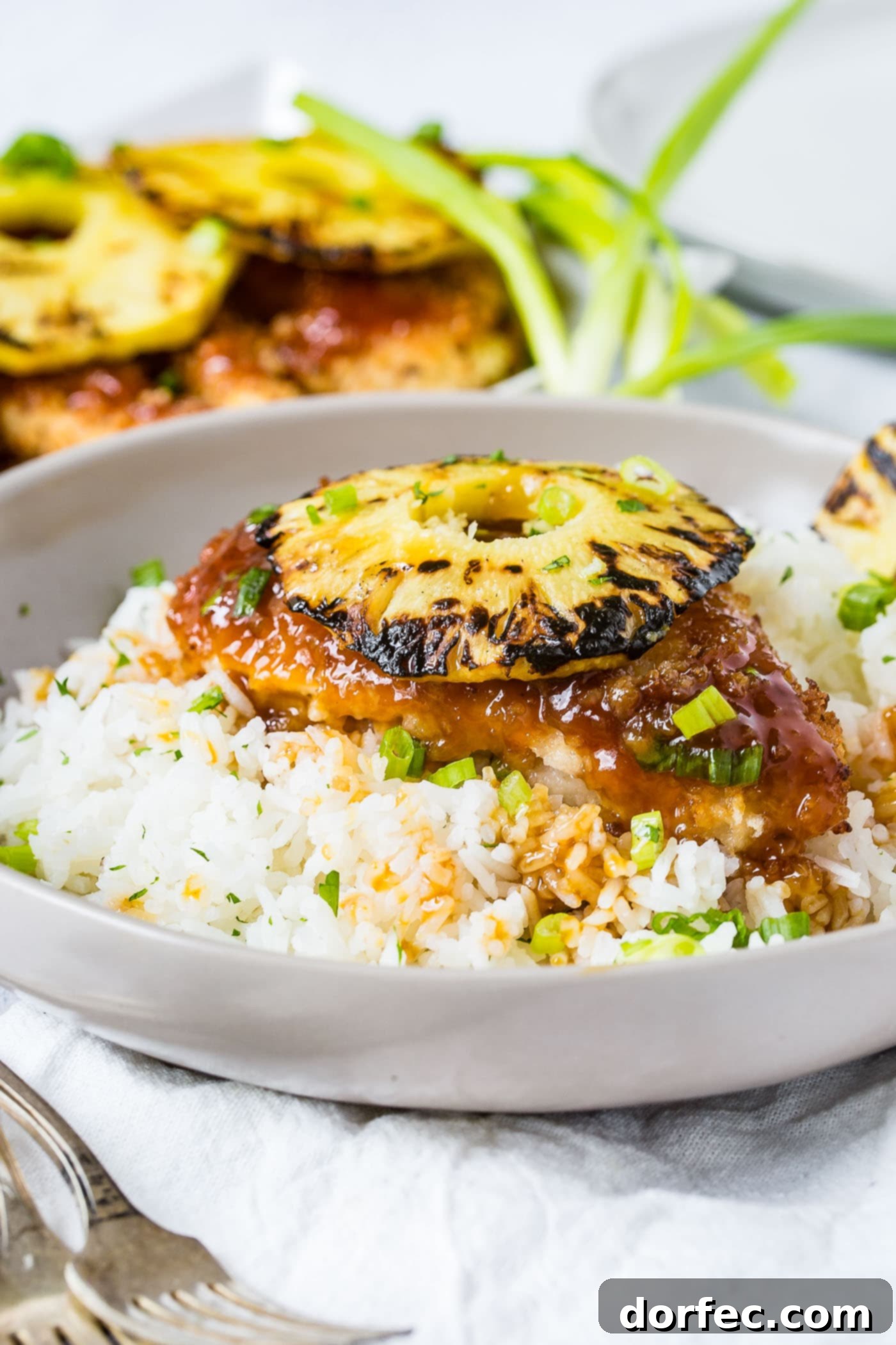 Sweet and Sticky Pineapple Chicken Dinner 2 A bowl of fluffy white rice topped with generous pieces of breaded sticky sweet and sour chicken, garnished with a beautifully grilled pineapple ring, creating an inviting and colorful dinner.