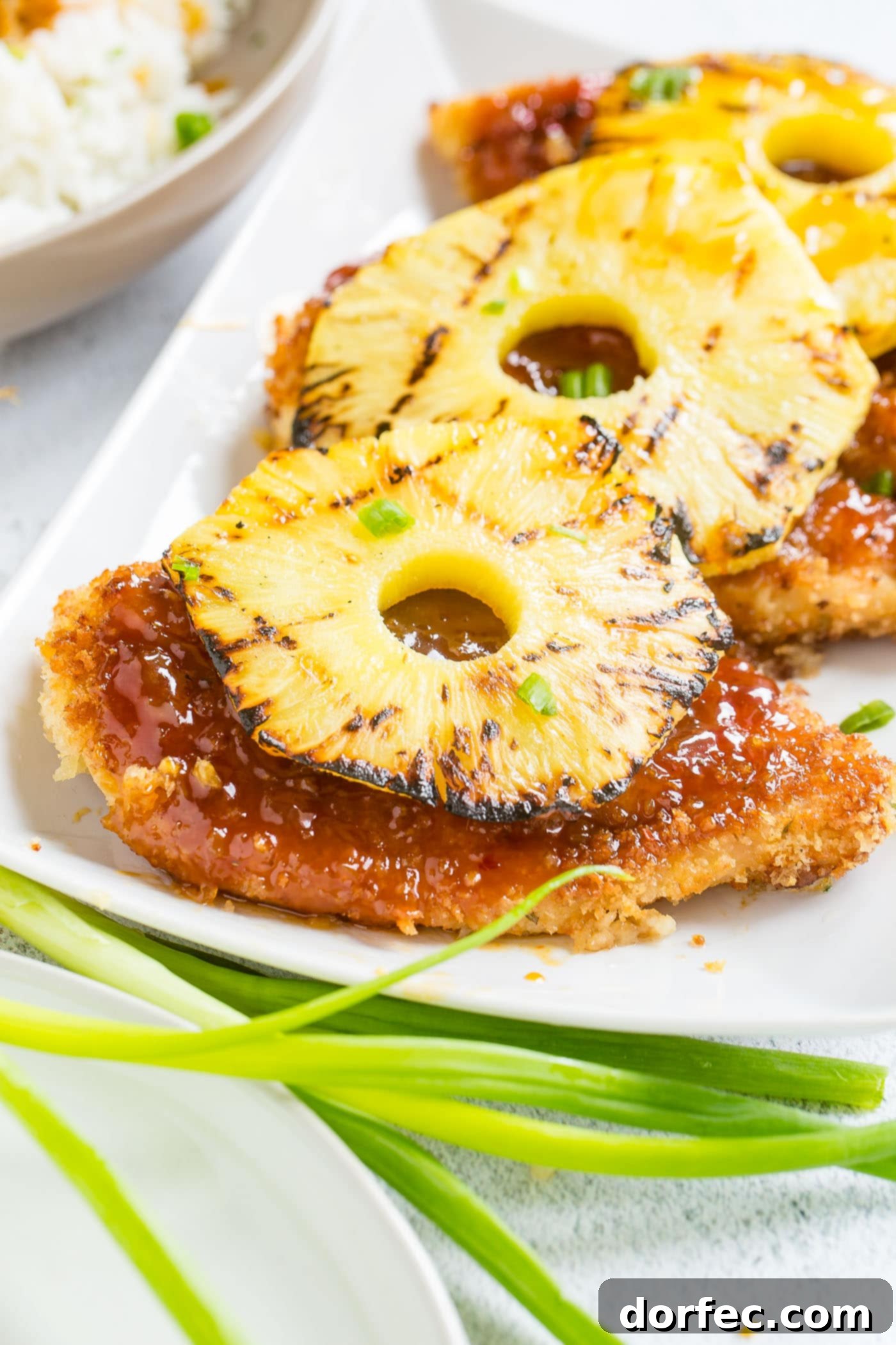 Sweet and Sticky Pineapple Chicken Dinner 3 Close-up of golden-brown breaded chicken pieces coated in a glossy, sticky sweet and sour sauce, with a perfectly grilled pineapple ring placed atop, ready to be served.