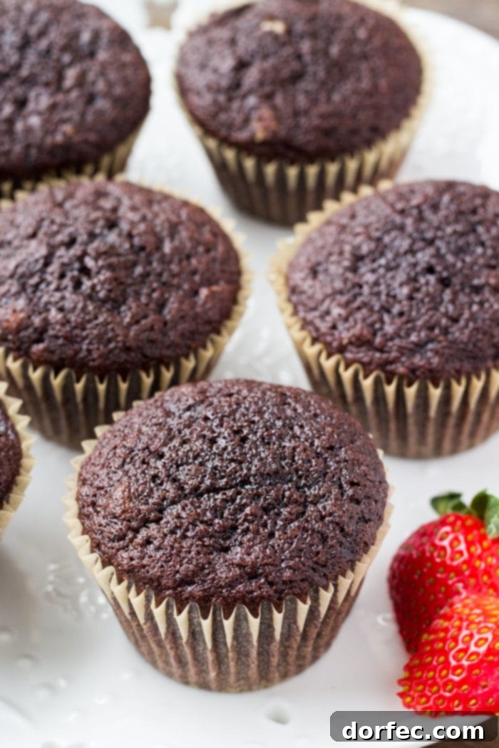 A photo of several freshly baked chocolate cupcakes, unfrosted and cooling on a wire rack, showcasing their perfectly domed tops and rich color.