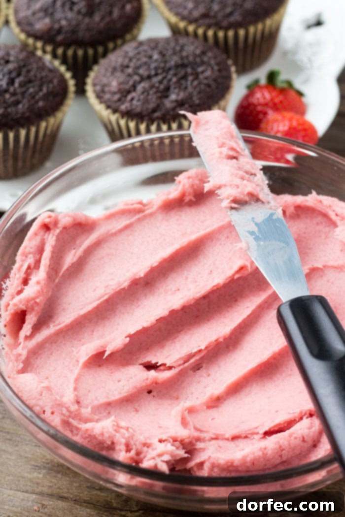 A close-up shot of freshly piped strawberry buttercream frosting on a chocolate cupcake, showcasing its vibrant pink color and creamy texture.