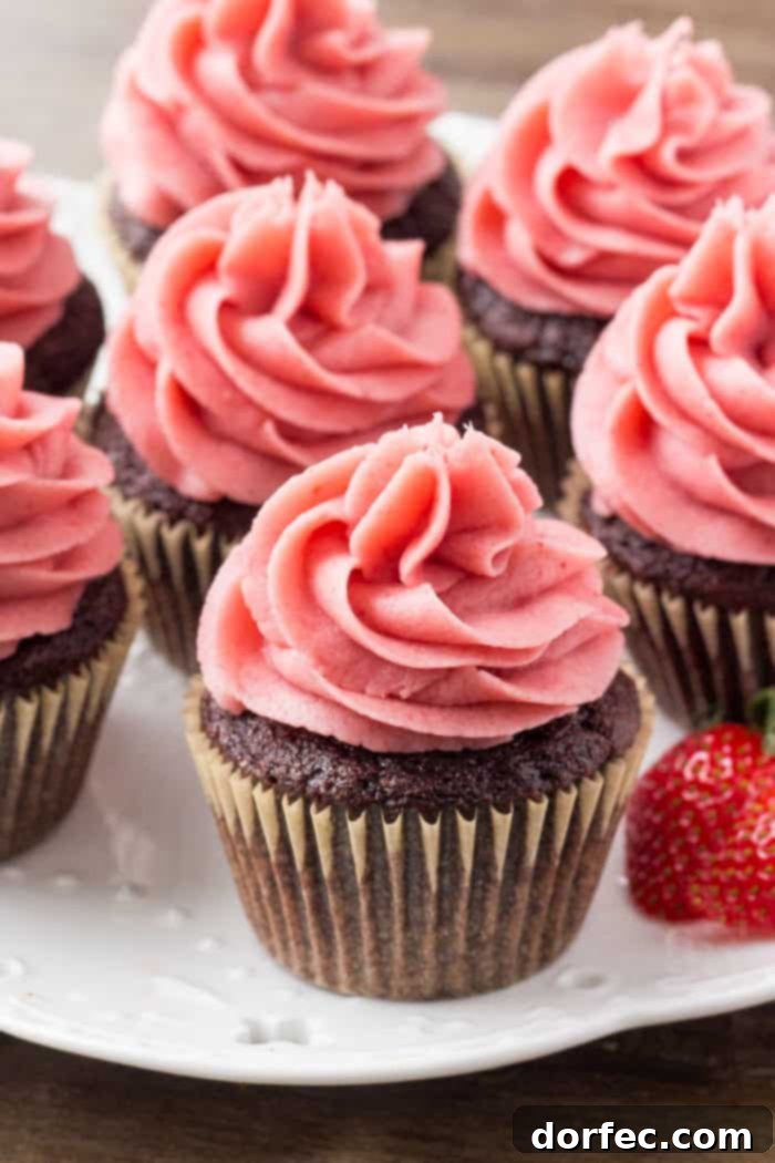 A beautifully frosted chocolate cupcake with bright pink strawberry frosting, ready to be enjoyed.