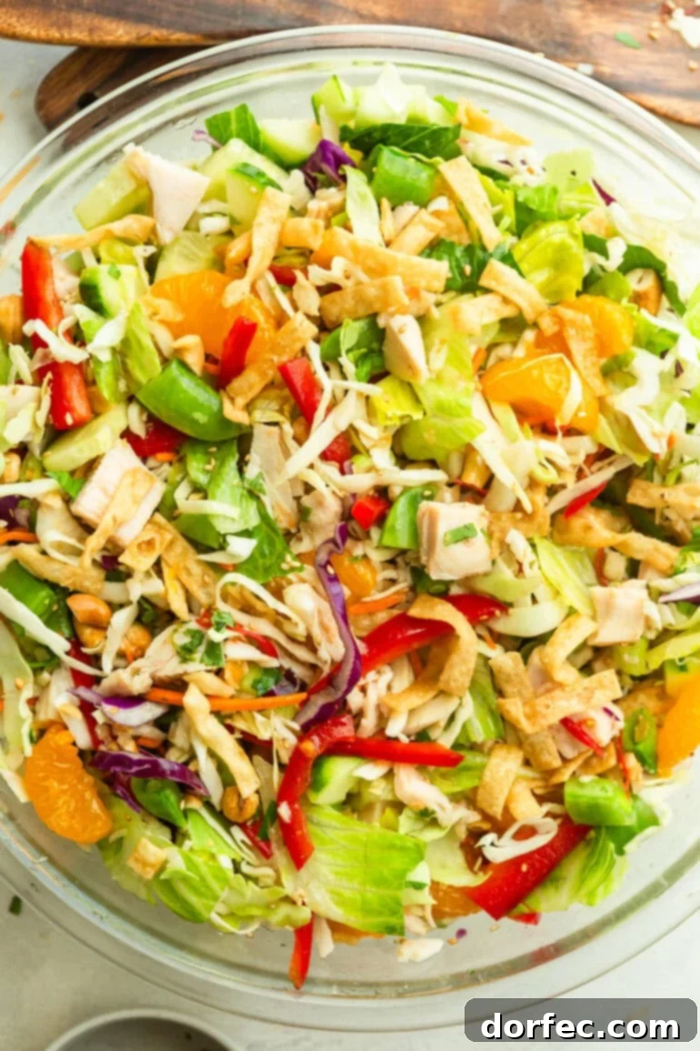 A large glass bowl filled with vibrant Wonton Chinese Chicken Salad, featuring shredded cabbage, bright mandarin oranges, thinly sliced red peppers, and crispy wonton strips on top.
