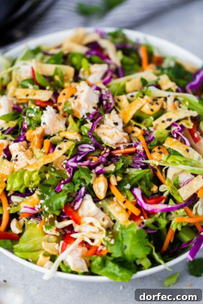 A vibrant close-up of a Wonton Chinese Chicken Salad, generously coated with a sesame seed dressing, highlighting the crisp textures and fresh ingredients.