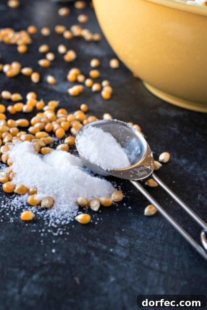 A measuring cup with salt and popcorn kernels spread out on the counter.