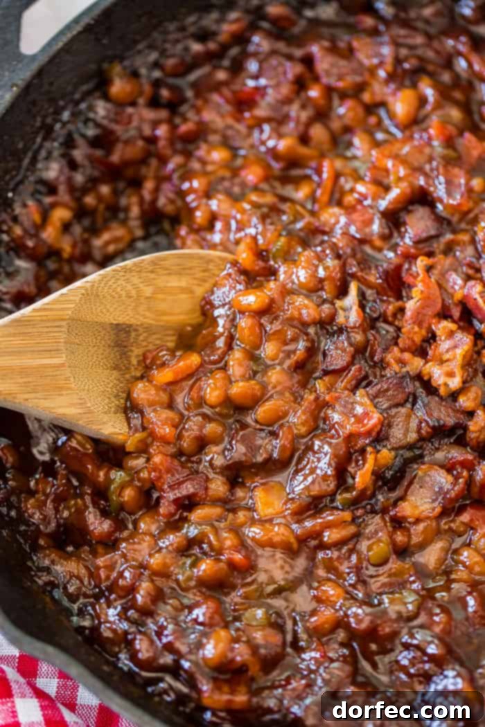 Old-Fashioned Homemade Baked Beans 3 A cast iron skillet with saucy baked beans and a wooden spoon