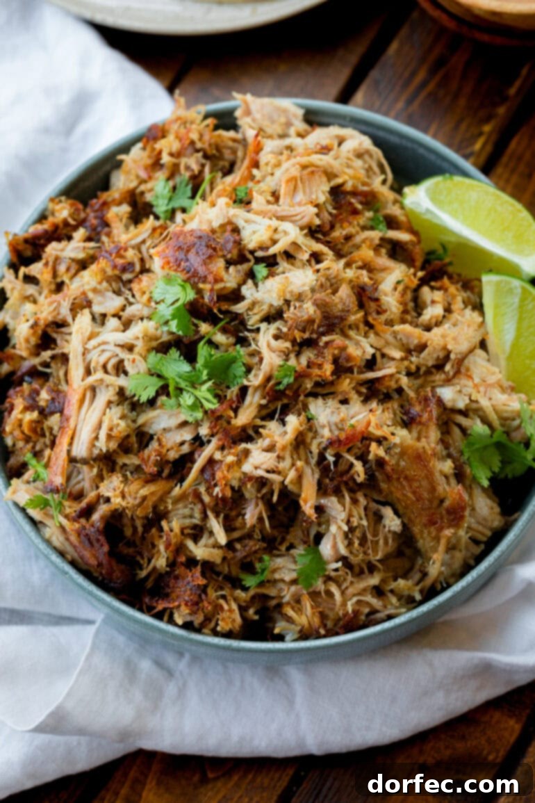 A close-up of a bowl filled with succulent shredded pork carnitas, garnished with fresh cilantro and accompanied by vibrant lime wedges, highlighting the rich flavors and inviting presentation. Keywords: easy carnitas recipe, prepare ahead carnitas, flavorful pork dish