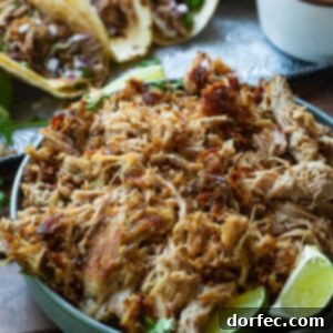 a photo of a bowl of shredded pork carnitas with three tacos in the background