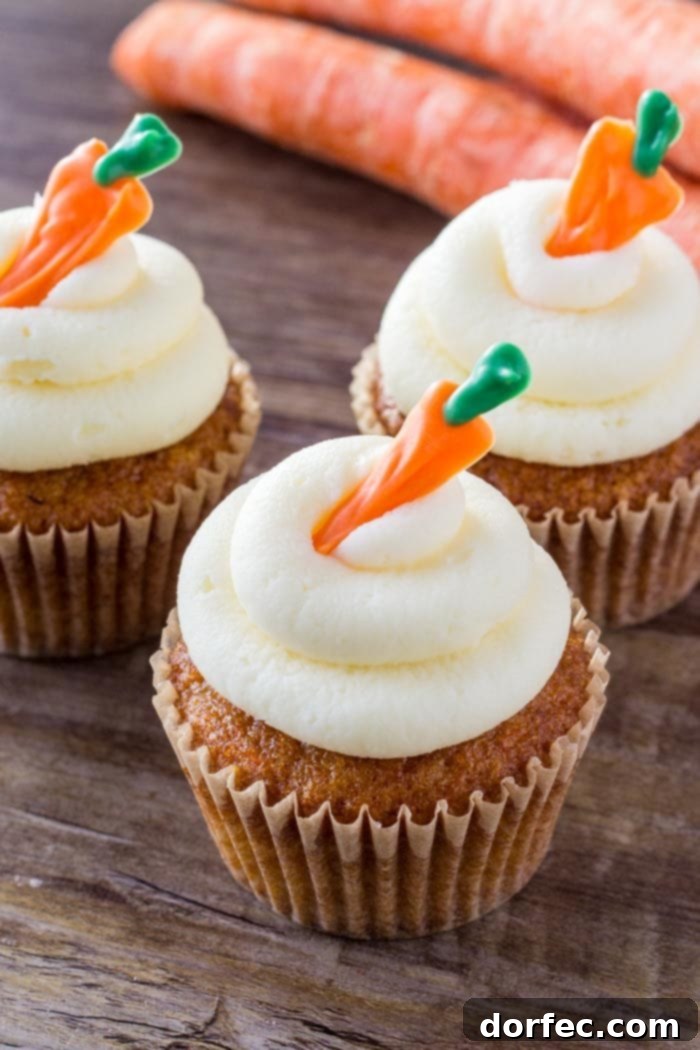 Three beautifully frosted carrot cake cupcakes with cream cheese frosting on a rustic wooden surface, invitingly ready to be enjoyed.