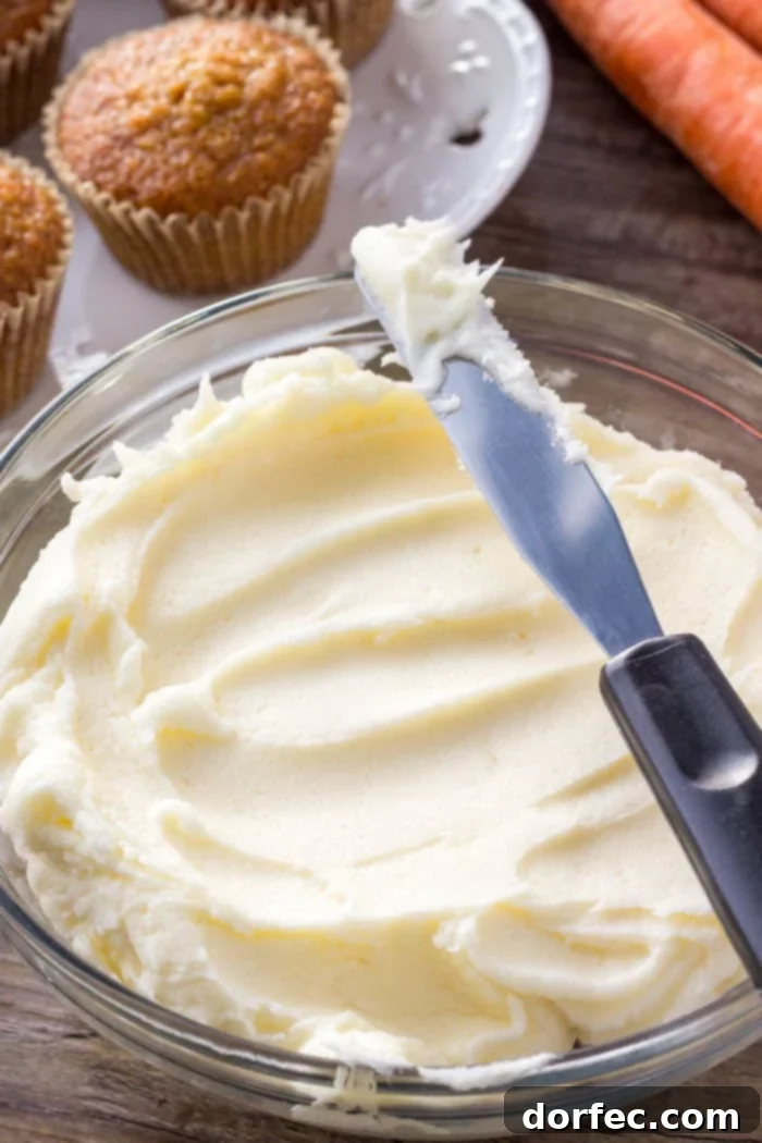A pristine bowl overflowing with creamy, smooth cream cheese frosting, ready to be swirled generously onto freshly baked carrot cake cupcakes.
