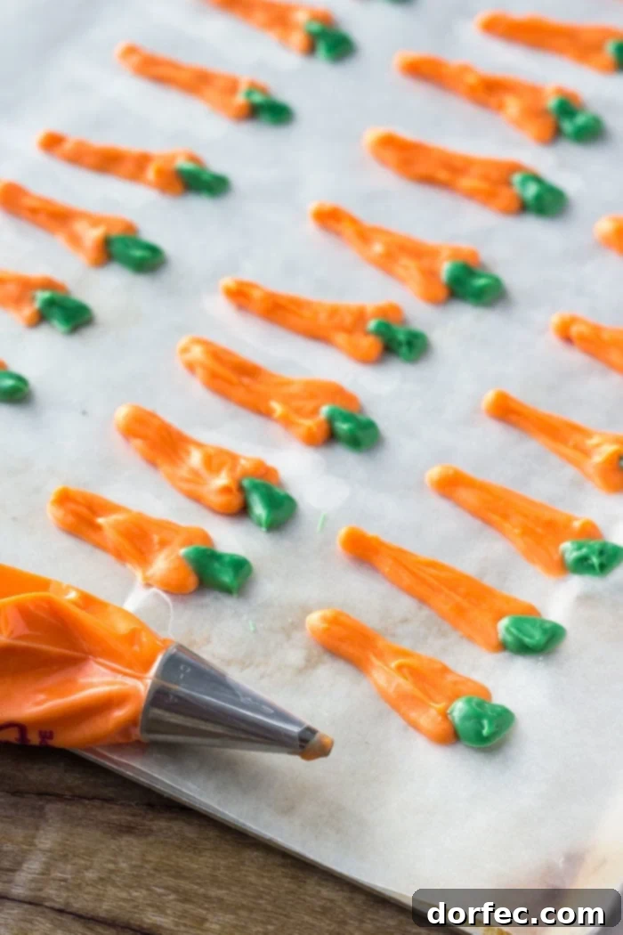 Delicate candy melt carrot toppers laid out on wax paper, featuring vibrant orange bodies and tiny green stems, ready to adorn freshly frosted carrot cake cupcakes.