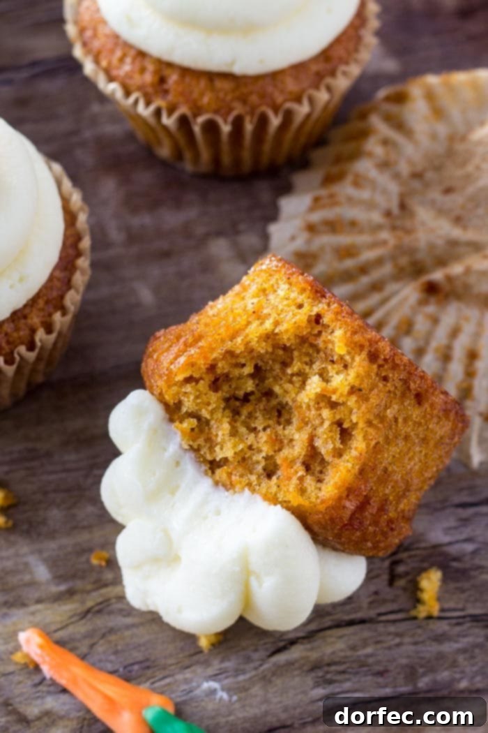 A delectable carrot cake cupcake, bitten to reveal its moist, spiced crumb and generously swirled with tangy cream cheese frosting, lying invitingly on its side.
