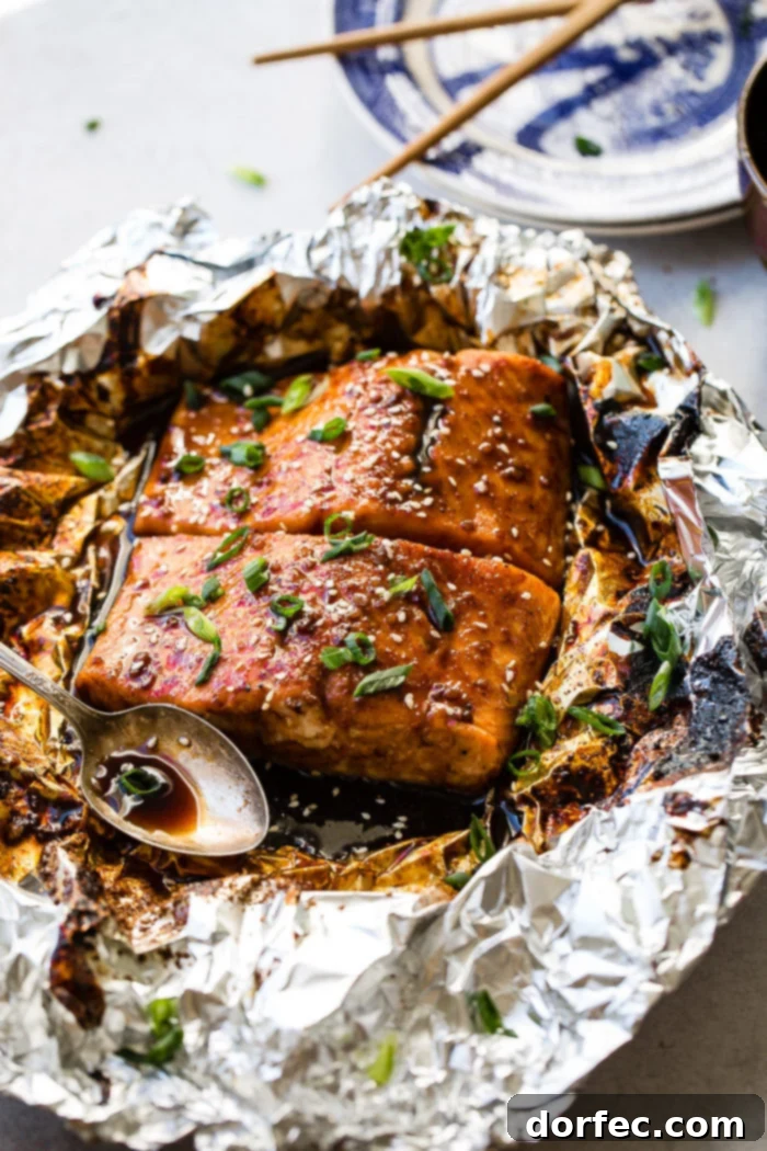 Sweet & Sticky Asian Salmon Packs 2 Two fillets of Asian Sticky Salmon in foil, garnished with green onions and sesame seeds, alongside a vintage spoon with sauce.