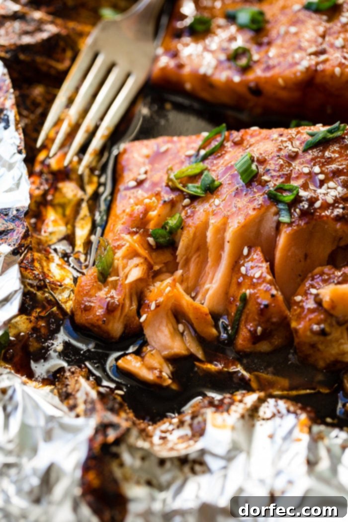 Sweet & Sticky Asian Salmon Packs 5 Two fillets of Asian Sticky Salmon in foil, garnished with green onions and sesame seeds, alongside a vintage spoon with sauce.