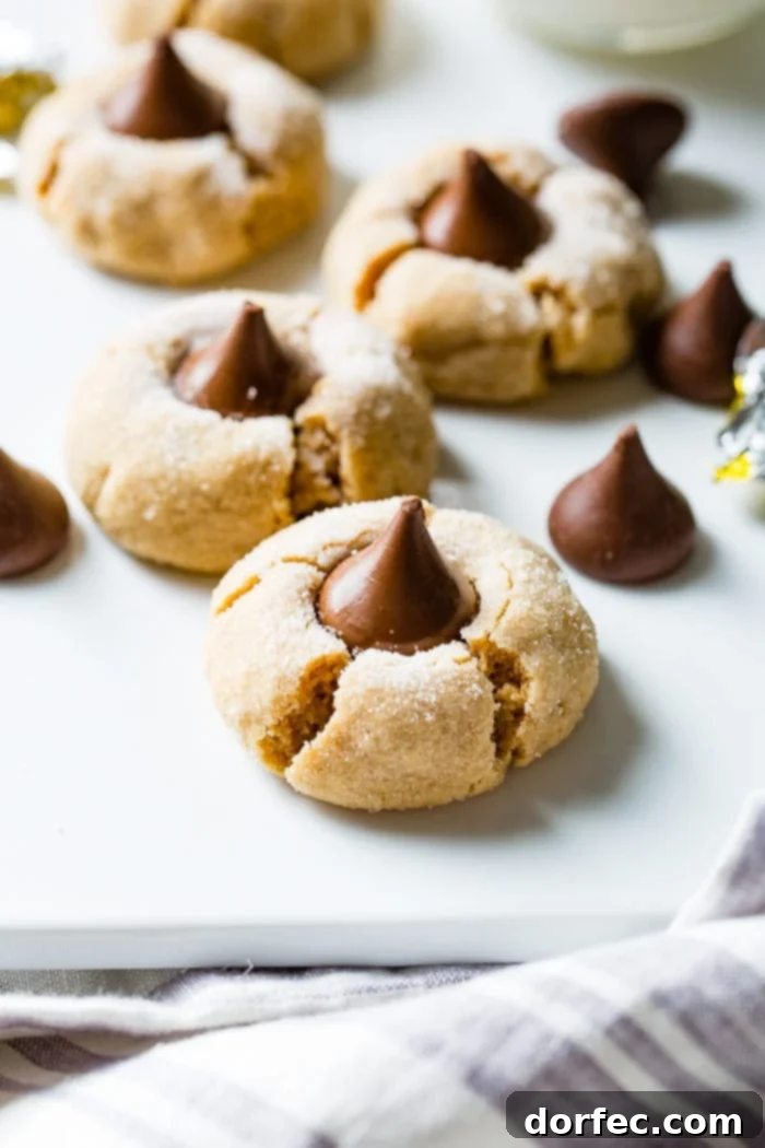 A selection of freshly baked Peanut Butter Blossom cookies arranged with several unwrapped Hershey's Kisses beside them, highlighting the chocolate element.