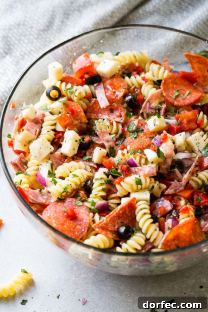 A glass bowl of quick and easy italian pasta salad recipe with homemade italian dressing. Rotini pasta with pepperoni, salsami, black olives, parmesan cheese, mozzarella cheese, peppers, dressing and red onions!