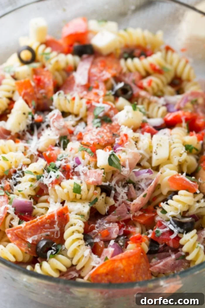 A glass bowl of quick and easy italian pasta salad recipe with homemade italian dressing. Rotini pasta with pepperoni, salsami, black olives, parmesan cheese, mozzarella cheese, peppers, dressing and red onions!