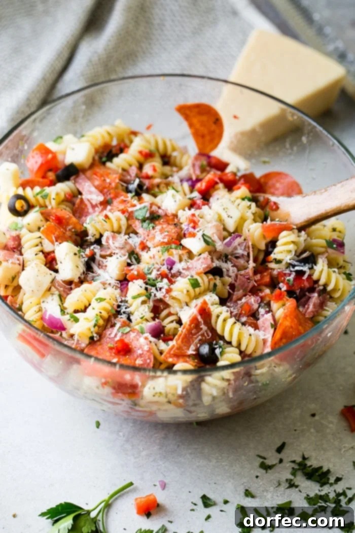 A glass bowl of quick and easy italian pasta salad recipe with homemade italian dressing. Rotini pasta with pepperoni, salsami, black olives, parmesan cheese, mozzarella cheese, peppers, dressing and red onions!