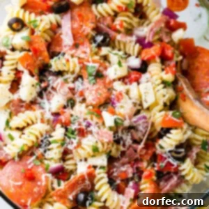 A glass bowl of quick and easy italian pasta salad recipe with homemade italian dressing. Rotini pasta with pepperoni, salsami, black olives, parmesan cheese, mozzarella cheese, peppers, dressing and red onions!