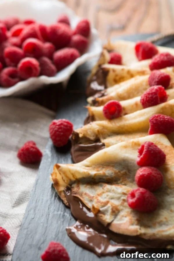 Nutella Crepes French breakfast, hazelnut, raspberry Close-up of a Nutella Crepe being rolled or folded, highlighting the creamy hazelnut filling