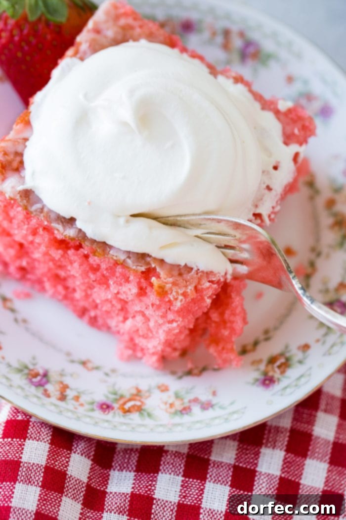 Strawberry Jiggle Cake 4 An overhead view of a perfectly baked slice of pink strawberries and cream jello cake, topped with a dollop of fluffy whipped cream, ready to be enjoyed. This fruit dessert is ideal for Mother's Day, spring, and summer gatherings.