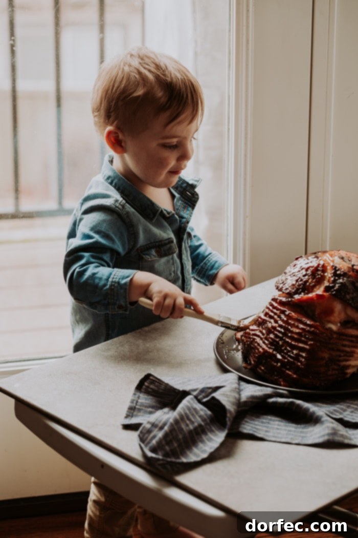A sweet toddler diligently brushing glaze onto a spiral ham, actively participating in the cooking process.