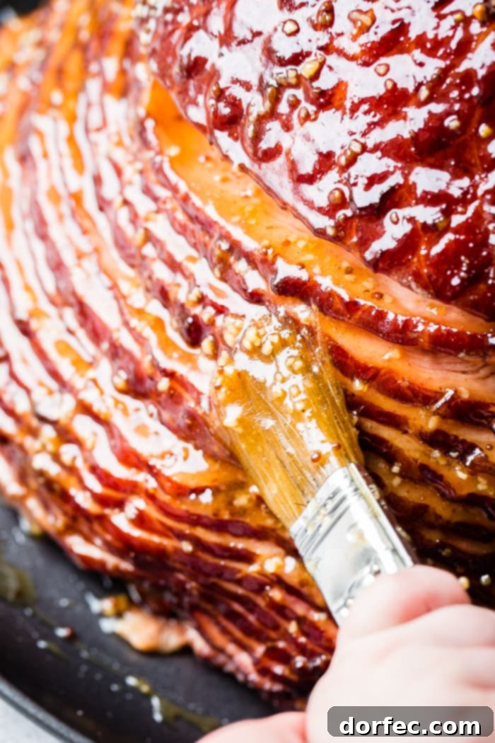 An inviting close-up of a succulent spiral ham, glistening with a rich garlic honey mustard glaze, presented on a dark serving platter with a basting brush nearby.