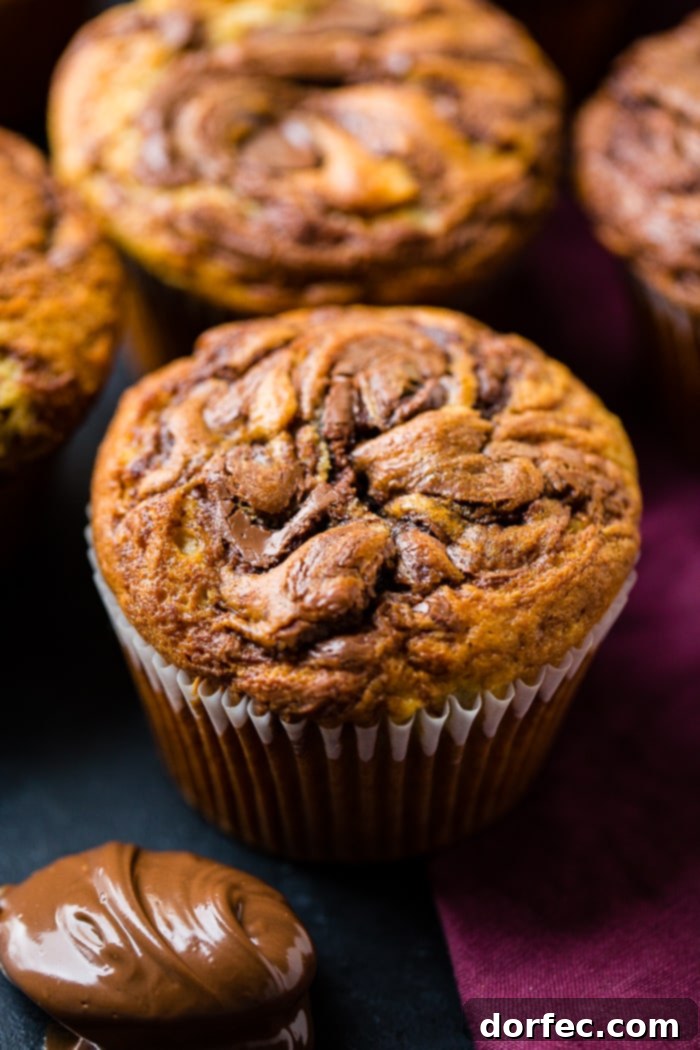 A golden-brown Nutella swirled banana muffin perfectly baked, surrounded by a delicious array of other muffins, ready to be enjoyed.