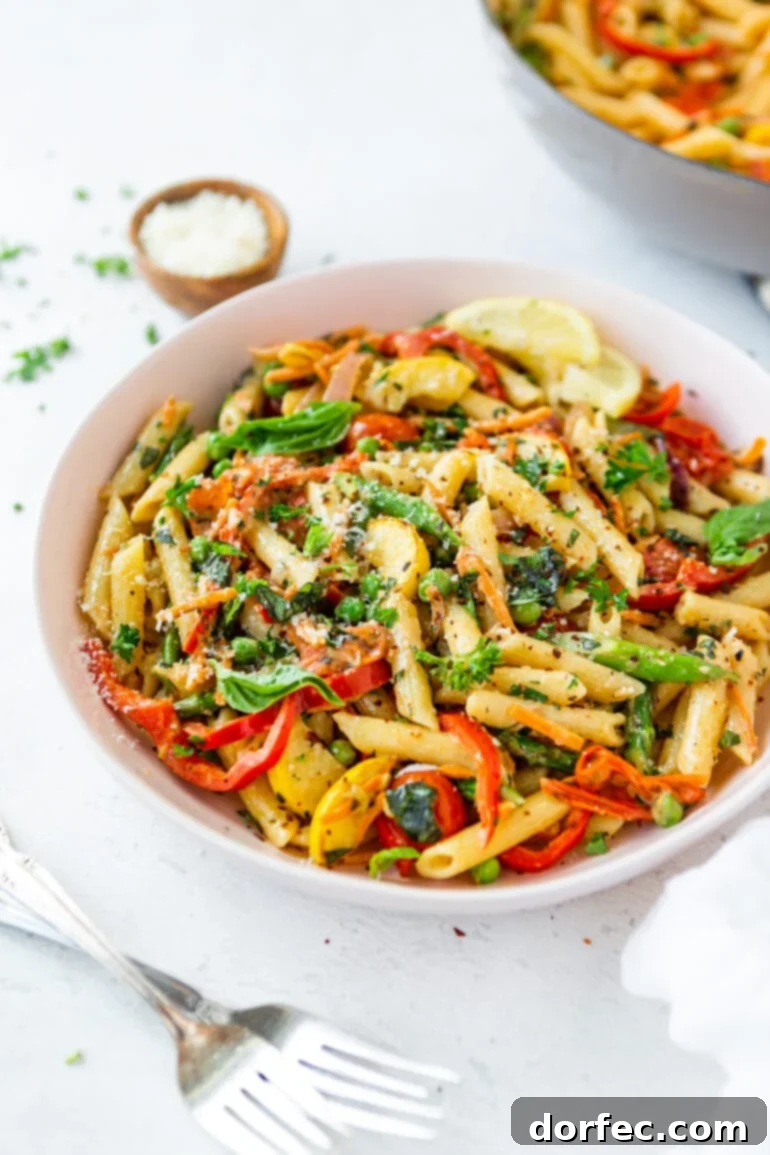 Vibrant Spring Pasta Primavera Recipe 3 A large white serving bowl filled with cooked penne pasta, generously tossed with fresh, bright vegetables and topped with a dusting of Parmesan cheese.