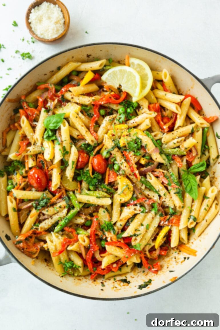 Vibrant Spring Pasta Primavera Recipe 4 A large white serving bowl showcases cooked penne pasta adorned with an abundance of fresh vegetables, aromatic herbs, and bright lemon slices, highlighting the dish's vibrant appeal.