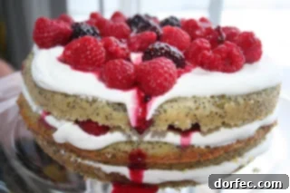 A beautifully layered Berry Crème Fraîche Cake adorned with fresh raspberries and blueberries.