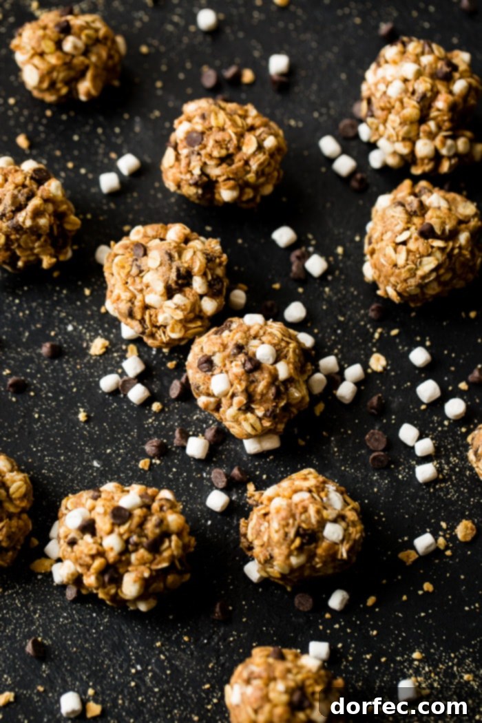 A black board with mini marshmallows, mini chocolate chips, and graham cracker crumbs sprinkled everywhere with protein no bake s'mores energy bites 