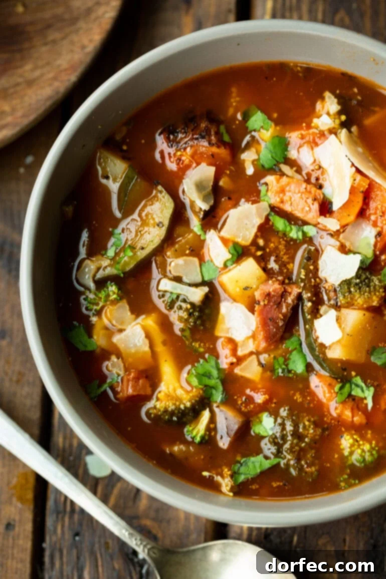 a photo of a bowl of hearty ham and vegetable soup loaded with potatoes, carrots, tomatoes, mushrooms and topped with chopped parsley