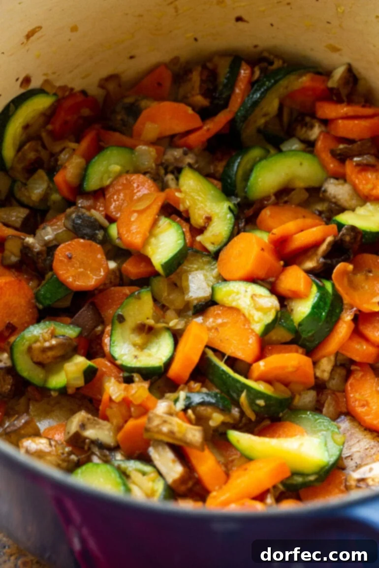 a photo of a zucchini, carrots, onions and mushrooms being sauteed in a dutch oven