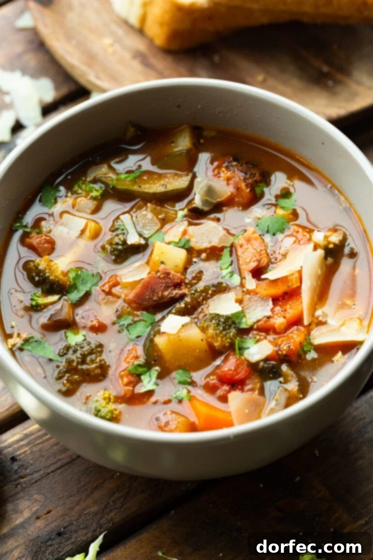 a photo of a large bowl bowl of ham and vegetable soup loaded with carrots, onions, tomatoes, mushrooms, broccoli and topped with shave parmesan
