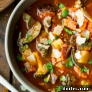 a photo of a bowl of hearty ham and vegetable soup loaded with potatoes, carrots, tomatoes, mushrooms and topped with chopped parsley
