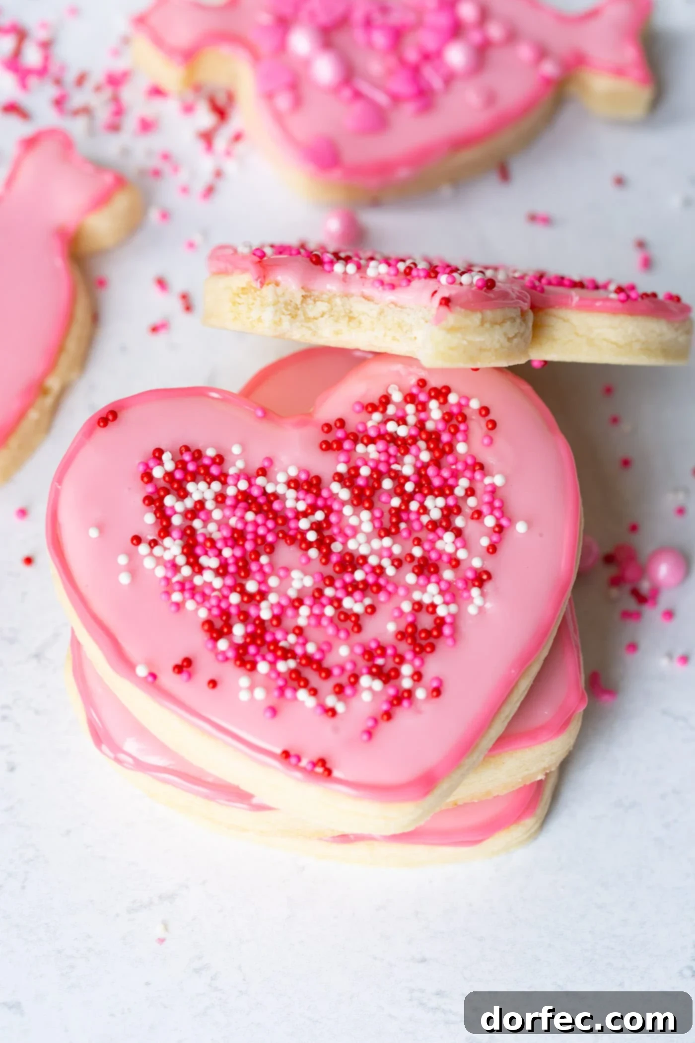 Classic Sugar Cookies 8 A close-up shot of a single, perfectly frosted pink heart-shaped sugar cookie with an assortment of colorful sprinkles, ready for a bite.