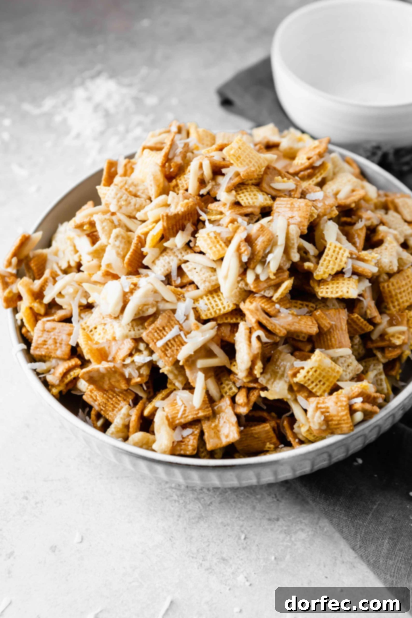 A closer view of the Sweet Chex Mix in a bowl, showcasing the glossy coating on the Corn Chex, Rice Chex, Golden Grahams, almonds, and coconut flakes, ready to be enjoyed as a party snack.