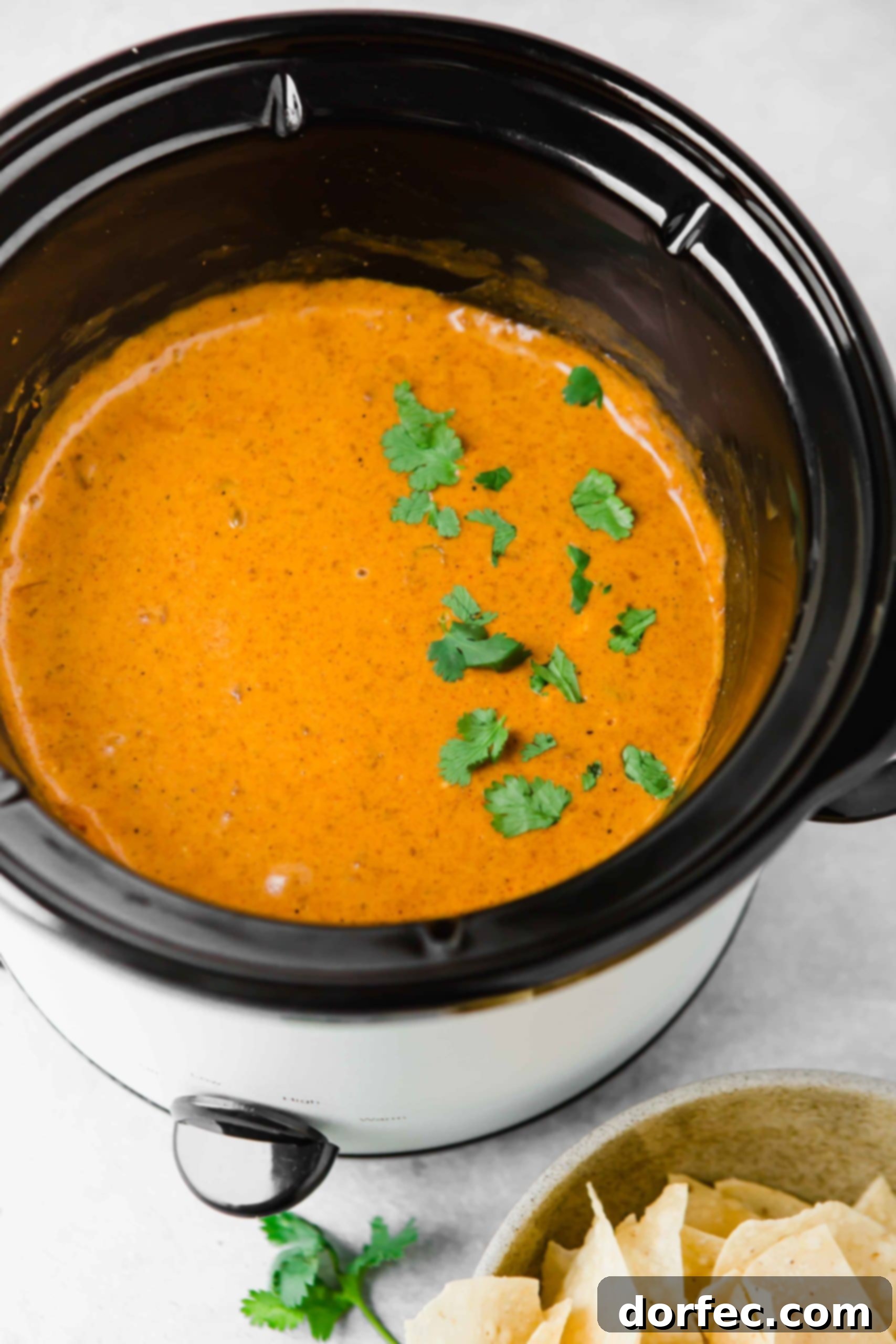 Chili’s Queso Dip A slow cooker full of chilis queso dip. there are a few parsley leaves scattered on top.