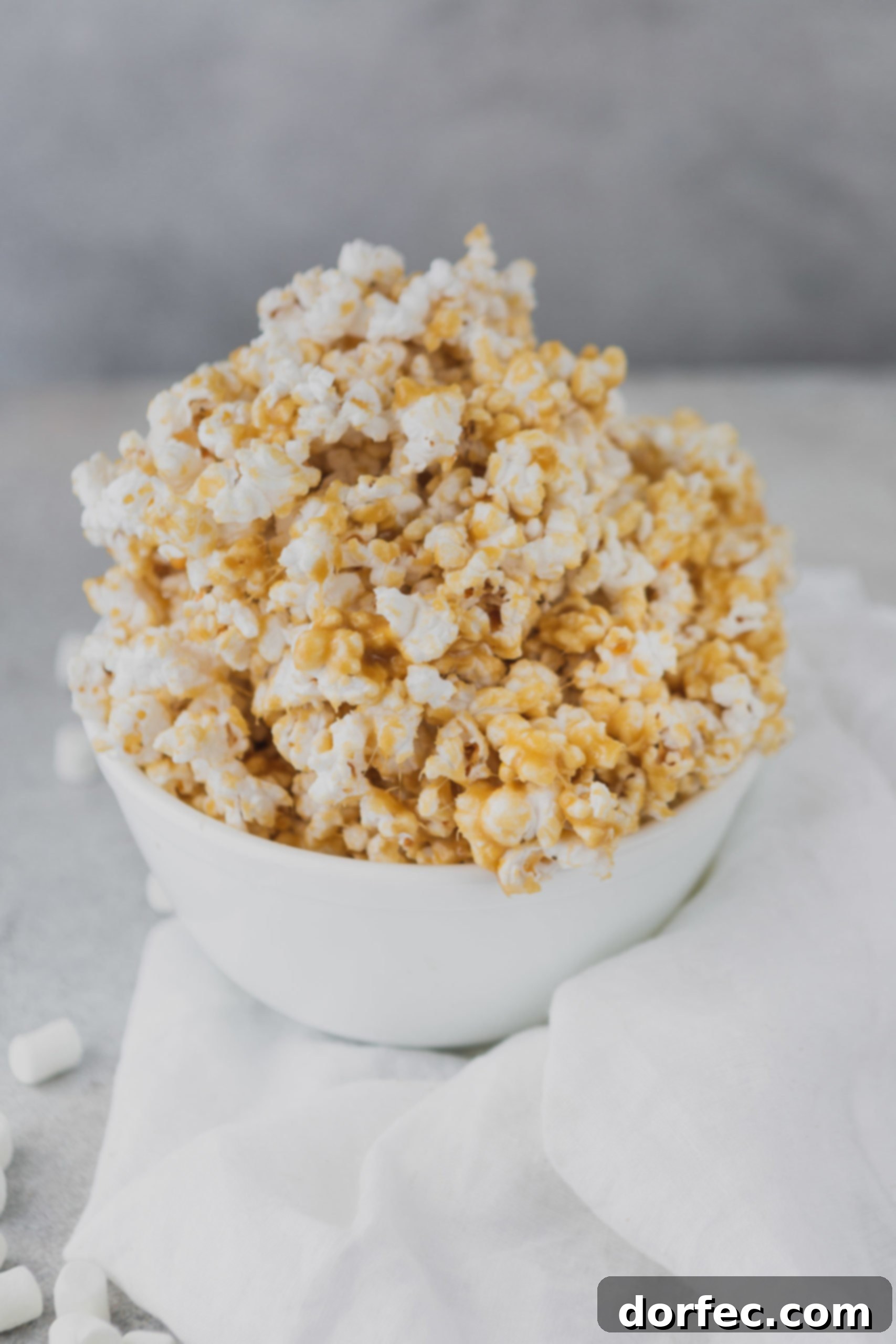 A crisp white bowl overflowing with golden, sticky caramel popcorn.
