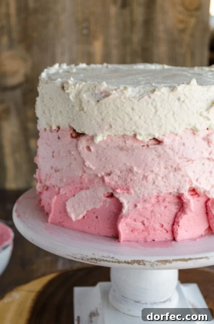 A three-layer cake is topped with three shades of pink frosting, each layer featuring a rustic, textured finish that adds charm and character. The frosting has yet to be smoothed, showing the potential for the ombre effect.