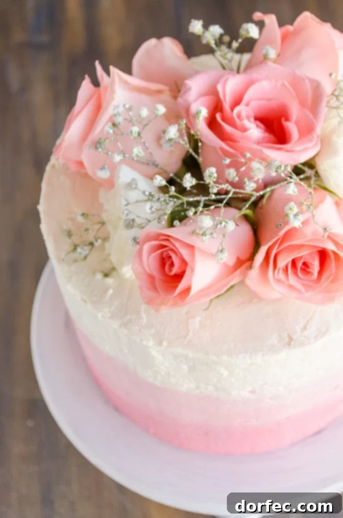 An overhead shot captures a stunning three-layer ombre Mothers Day strawberry cake, adorned with fresh pink roses and sparkling sprigs of baby's breath, ready for celebration.