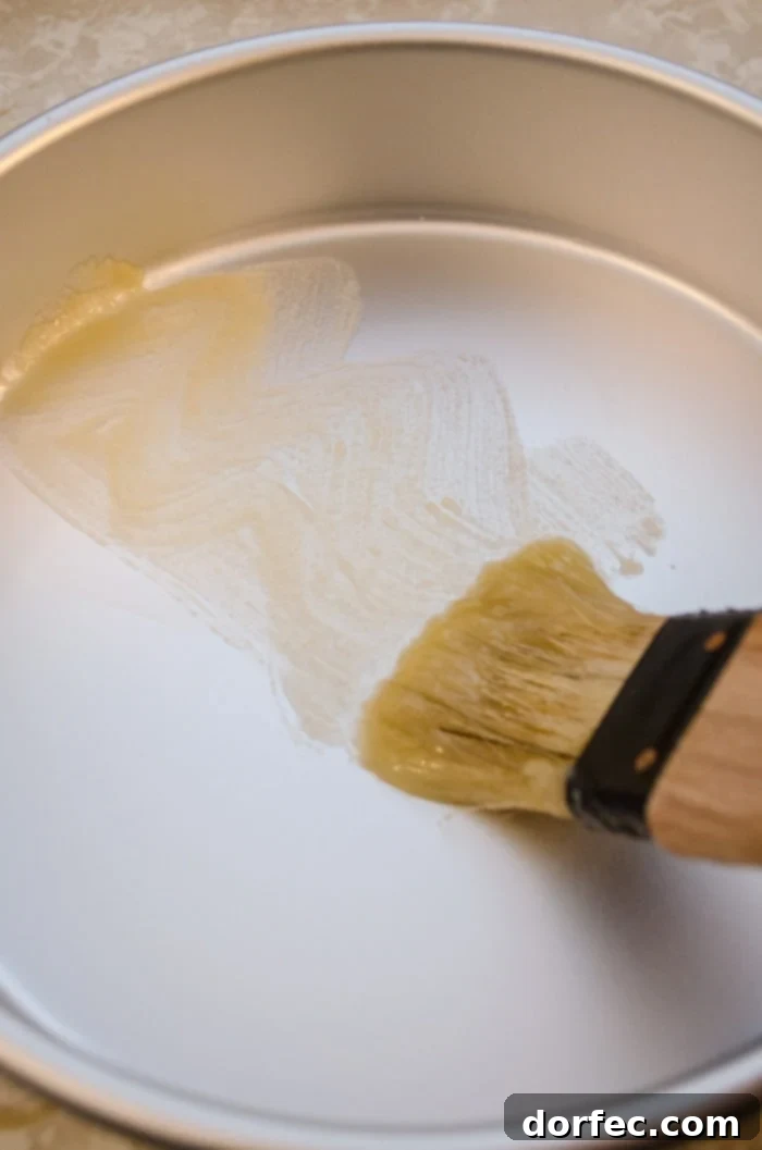 A brush coated with a smooth paste made from equal parts melted butter and flour glides over a gleaming metal cake pan, ensuring a perfectly non-stick surface for the cake.