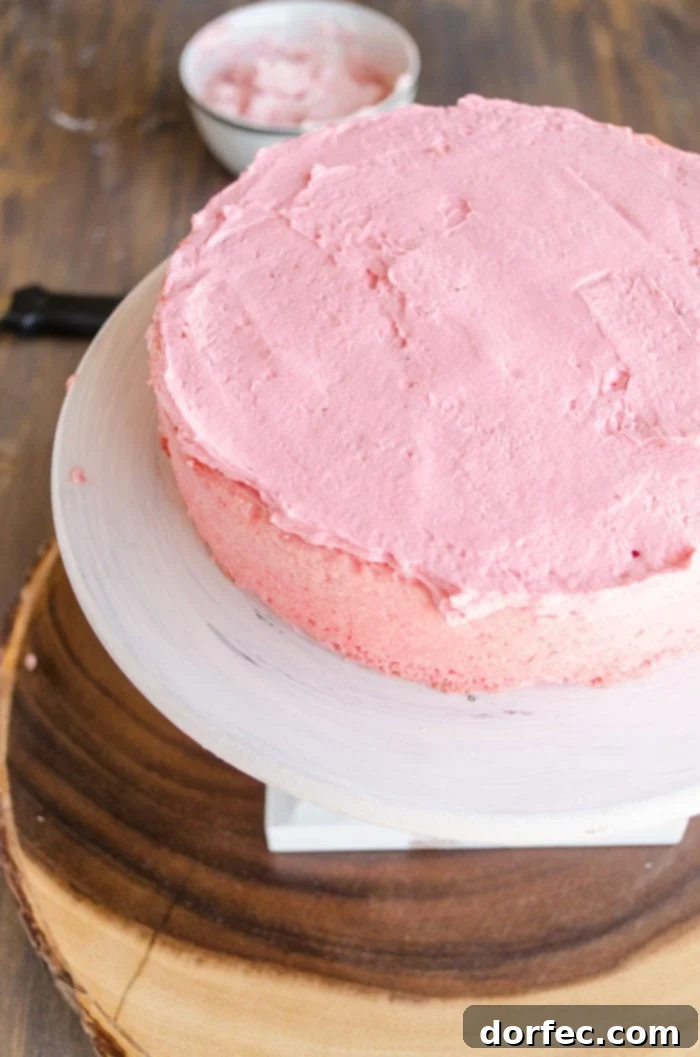 The darkest pink layer of this cake is placed on a raised cake stand and topped with a matching dark pink frosting, ready for the next layer.